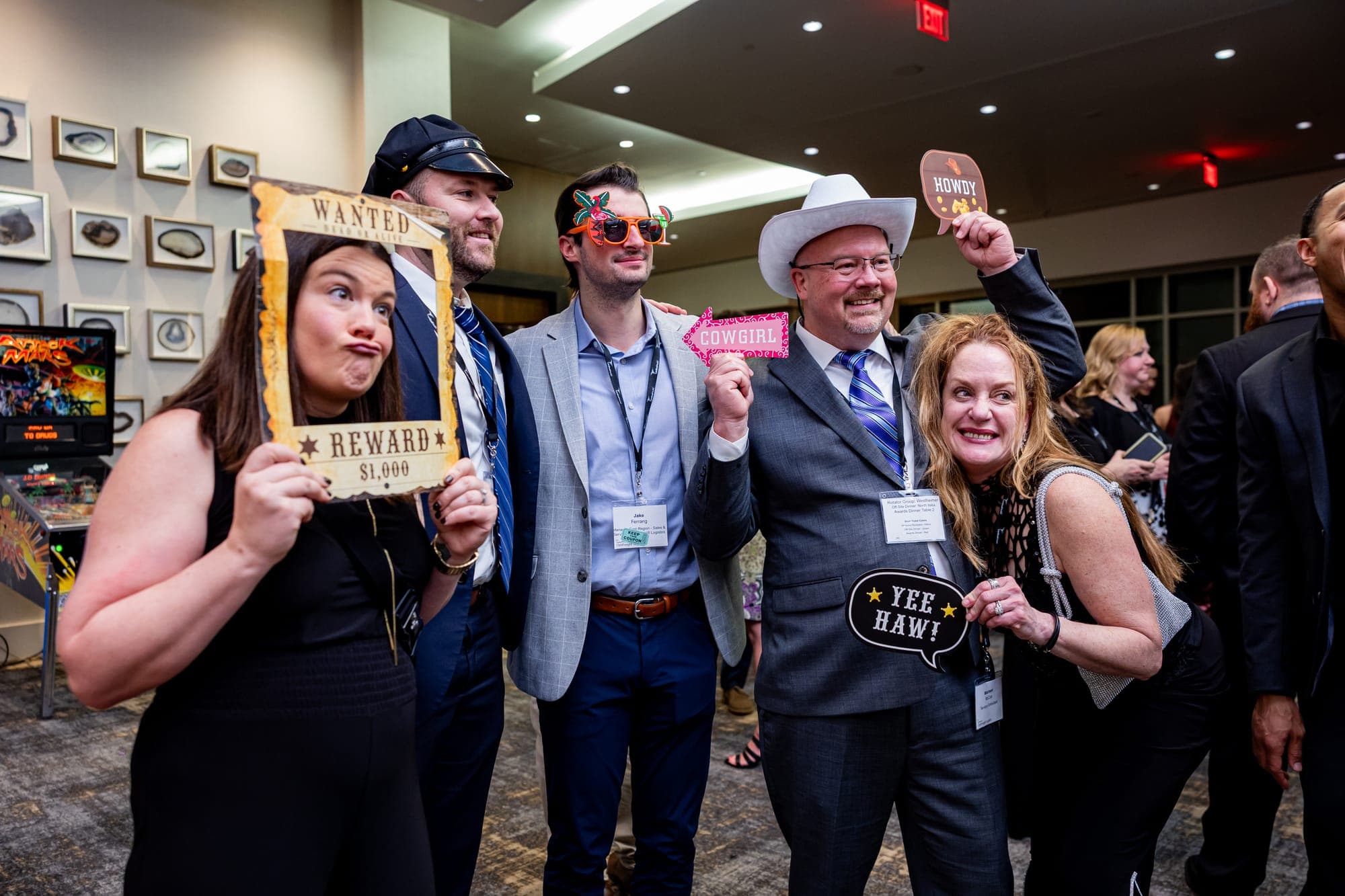 Five guests holding props, a Wanted poster frame and a cowboy hat among them, on the event floor